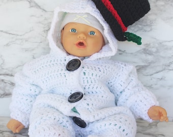 May include: A white crocheted snowman outfit with a black top hat and green trim. The outfit has a hood and buttons down the front.