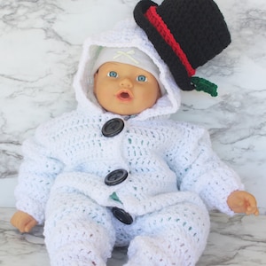 May include: A white crocheted snowman outfit with a black top hat and green trim. The outfit has a hood and buttons down the front.