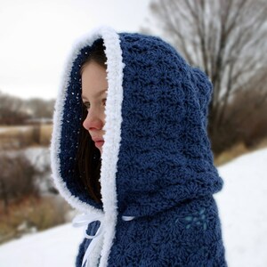 K&ouml;nnte beinhalten: Eine blaue, geh&auml;kelte Kapuzenjacke mit wei&szlig;em Besatz. Die Jacke wird von einer Person mit langen braunen Haaren getragen.