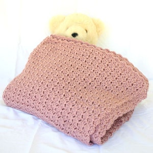 May include: A soft, pink crocheted blanket with a teddy bear peeking out from under it.