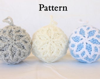 Könnte beinhalten: Drei gehäkelte Ornamente in verschiedenen Farben und Mustern. Das Ornament links ist grau, das mittlere Ornament ist weiß und das Ornament rechts ist blau mit einem weißen Schneeflockenmuster.