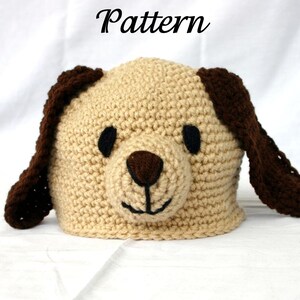 Op de afbeelding: Een gehaakte hondenmuts in beige, bruin en zwart. De muts heeft een honden gezicht met flaporen, een bruine neus en zwarte ogen. Het woord "Pattern" staat in zwart schrift bovenaan.