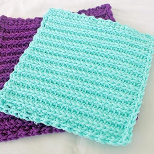 May include: Two handmade crochet washcloths. One is a vibrant turquoise, the other a deep purple. Both are square with a textured, ribbed pattern. The washcloths are made of soft yarn, perfect for gentle cleansing.