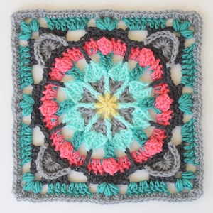 May include: A crocheted square with a colorful geometric pattern in shades of teal, pink, gray, and yellow. The center of the square features a starburst design.