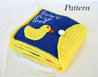 May include: A crocheted baby book with a yellow duck on the front cover. The book is blue and yellow and has a button closure. The text on the cover reads "Baby's First Book".