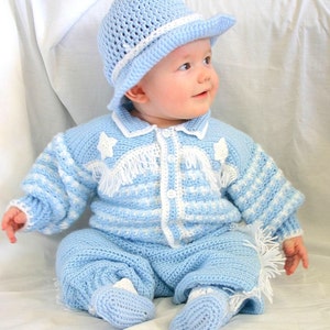 May include: A baby wearing a blue crocheted outfit with white accents. The outfit includes a long-sleeved shirt, pants, and booties. The baby is also wearing a blue crocheted cowboy hat.