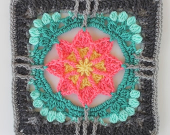 May include: A square crochet motif featuring a central yellow and coral star-shaped flower pattern. The flower is surrounded by a teal border with textured clusters, framed by a dark gray outer square with light gray edging.