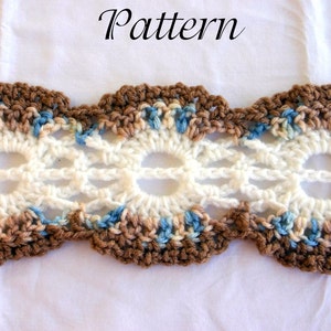 May include: A close-up of a crocheted lace trim with a brown, blue, and white color scheme. The trim features a repeating pattern of scalloped edges and openwork designs.