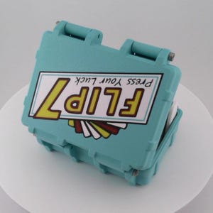 May include: A teal-colored, hinged case with the text "FLIP 7" in yellow and brown, and "Press Your Luck" above. The case is open, revealing a white interior. The design includes a retro-style graphic.