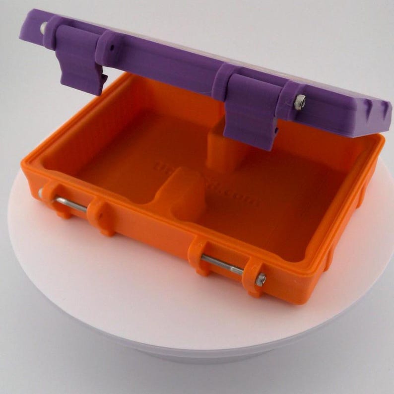 May include: An open orange and purple plastic container with a hinged lid. The container has a rectangular shape with rounded corners and metal bar closures. The lid is purple and the interior is orange.
