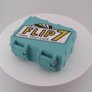 May include: A teal-colored rectangular box with the text "FLIP 7 Press Your Luck" on the top. The box has a hinged lid and two silver clasps. The box is sitting on a white surface.