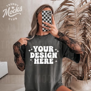 May include: A dark gray oversized t-shirt with a white graphic that says "YOUR DESIGN HERE" with stars on either side of the text. The model is wearing the t-shirt with black lace sleeves and white jeans.