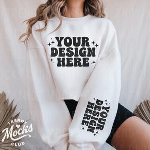 Peut inclure: Sweat-shirt blanc à manches longues et coupe courte. Le sweat-shirt comporte un texte noir qui dit "YOUR DESIGN HERE" sur le devant et "YOUR DESIGN HERE" sur les manches.