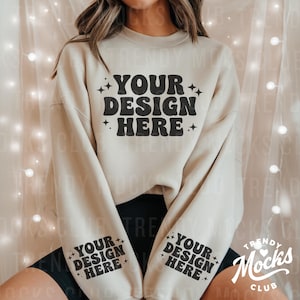 May include: A beige sweatshirt with long sleeves and a crew neck. The sweatshirt has the text "YOUR DESIGN HERE" printed on the front in black. The sleeves have the text "YOUR DESIGN HERE" printed on the cuffs in black.