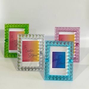 May include: Four small picture frames in shades of green, clear, pink, and blue. Each frame has a square shape with a textured, bubble-like border. The frames hold colorful gradient art with the text "The Creative Statement".
