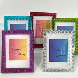 May include: A collection of colorful picture frames in teal, red, green, purple, and clear. Each frame has a beaded border and contains a print with the text "The Creative Statement" in a gradient color scheme.