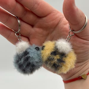 May include: Two fuzzy bee-shaped keychains. One is gray and black, the other is yellow, black, and white.