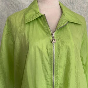 May include: A bright lime green jacket with a collared neckline and a silver zipper. The zipper pull features the letters "DVF". The jacket is made of a lightweight, slightly textured material.