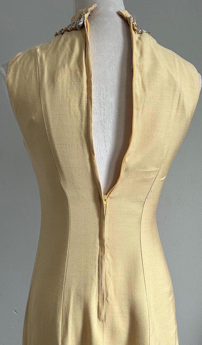May include: A sleeveless, pale yellow dress with a high neckline and a back zipper. The dress is fitted and appears to be made of a smooth fabric. The neckline is embellished with a decorative trim.