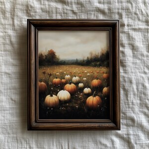 May include: A framed print depicting a field of pumpkins in shades of orange and white. The artwork has a soft, painterly style, set within a dark brown wooden frame. The background shows a cloudy sky and trees.