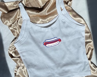Può includere: Canotta bianca con grafica Chicago Baseball hot dog. La grafica presenta un hot dog rosso e blu con le parole "Chicago Baseball" in un ovale blu. La canotta è realizzata in un materiale morbido e leggero.