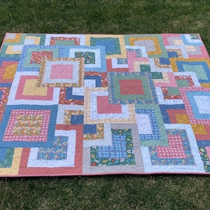 May include: A patchwork quilt with a geometric design featuring squares and rectangles in shades of pink, blue, green, and yellow.