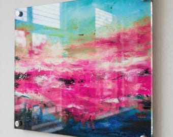 May include: A rectangular acrylic wall art piece featuring an abstract painting with vibrant layers of hot pink, bright turquoise, and deep navy blue. The artwork is mounted with four silver-toned metal standoffs at each corner, creating a glossy finish.