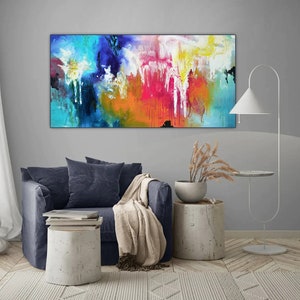 K&ouml;nnte beinhalten: Abstraktes Gem&auml;lde mit leuchtenden Farben in Blau, Gelb, Orange, Rosa und Wei&szlig;. Das Gem&auml;lde h&auml;ngt an einer grauen Wand &uuml;ber einem blauen Sofa mit einer Wolldecke.