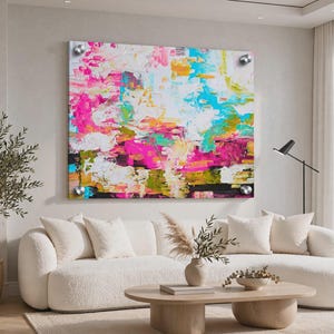 May include: A large rectangular wall art piece featuring an abstract painting with vibrant splashes of hot pink, bright turquoise, sunny yellow, and white. The artwork is mounted with four silver circular standoffs at each corner of the frame.