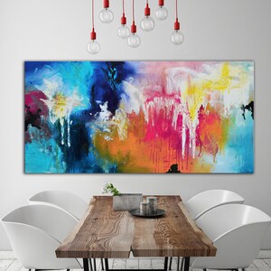 K&ouml;nnte beinhalten: Abstraktes Gem&auml;lde mit leuchtenden Farben in Blau, Rosa, Gelb, Orange und Wei&szlig;. Das Gem&auml;lde h&auml;ngt an einer wei&szlig;en Wand &uuml;ber einem Holztisch mit zwei wei&szlig;en St&uuml;hlen.