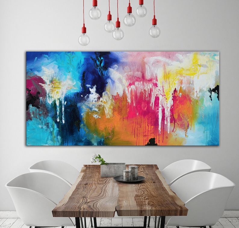K&ouml;nnte beinhalten: Abstraktes Gem&auml;lde mit leuchtenden Farben in Blau, Rosa, Gelb, Orange und Wei&szlig;. Das Gem&auml;lde h&auml;ngt an einer wei&szlig;en Wand &uuml;ber einem Holztisch mit zwei wei&szlig;en St&uuml;hlen.