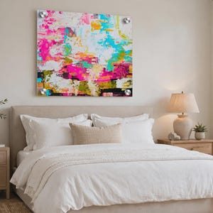 May include: A square acrylic wall art piece featuring an abstract painting with vibrant splashes of hot pink, bright turquoise, sunny yellow, and deep black against a white background, mounted with four silver circular hardware standoffs.