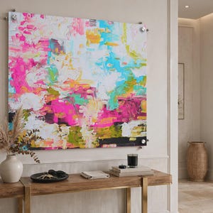 May include: A large square abstract wall art piece mounted with silver hardware, featuring thick, textured brushstrokes in vibrant shades of hot pink, bright turquoise, sunny yellow, white, and deep black, creating a bold, layered composition.