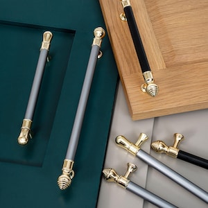 May include: Assortment of cabinet hardware pulls in various finishes.  The pulls are made of metal and have a gold finish.  Some pulls are gray, while others are black.