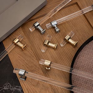 May include: A set of clear acrylic cabinet hardware with gold and silver accents. The hardware includes pulls and knobs in various styles.