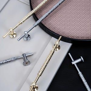 May include: Four different cabinet door pulls with a textured design. Two are gold, one is silver, and one is chrome. The pulls are on a white and black background.