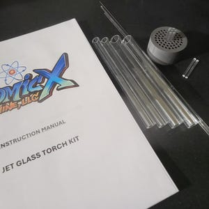 May include: A 7-jet glass torch kit with instructions. The kit includes a clear glass torch with a metal base, seven glass tubes, and a metal cap. The instructions are printed on a white booklet with a colorful logo.