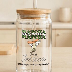 May include: A clear glass jar with a bamboo lid and a straw. The jar has a green and white graphic of a bull with the text "MATCHA" repeated three times. The text "Taurus, Jessica" and the quote "Stubborn, Smuggly, and Always Smelling like Fresh Flowers" are also printed on the jar.