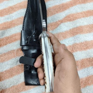 Puede incluir: Un cuchillo de caza con una hoja de acero pulido y un mango de hueso y material marr&oacute;n oscuro. El cuchillo va acompa&ntilde;ado de una funda de cuero negro con trabilla para cintur&oacute;n y cierre de bot&oacute;n a presi&oacute;n.