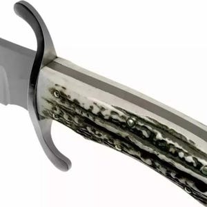 Puede incluir: Primer plano de un cuchillo de caza grande. La hoja es plateada, y el mango es una mezcla de blanco y marr&oacute;n oscuro, con una franja gris oscura en el centro. La guarda es curva y negra.