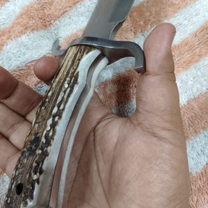 Puede incluir: Un cuchillo de caza grande con una hoja de acero inoxidable y un mango de asta y material blanco. El mango est&aacute; asegurado con remaches de lat&oacute;n. El cuchillo tiene una guarda curva.
