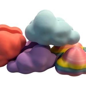 May include: A collection of colorful cloud-shaped objects in shades of red, purple, blue, and rainbow. The objects are stacked and appear to be made of a solid material, possibly plastic or resin. The rainbow cloud has stripes.