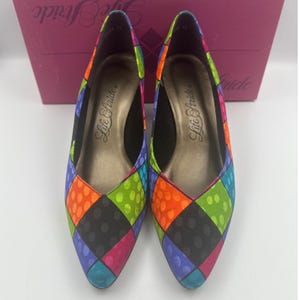 May include: A pair of Life Stride brand women's flats with a colorful patchwork design. The flats feature a pointed toe and a low heel. The patchwork pattern includes squares of black, orange, green, blue, and pink with polka dots.