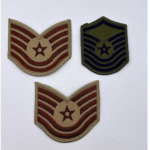 May include: Three military patches. Two are tan and brown with a star in the center and horizontal stripes. The third is green and navy blue with a star and horizontal stripes. All have a curved top.