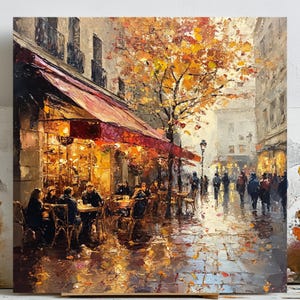 Könnte beinhalten: Ölgemälde einer Pariser Cafészene. Das Kunstwerk zeigt eine rote Markise über einem Café mit Gästen an Tischen. Ein Baum mit orangefarbenen Blättern und eine nasse Kopfsteinpflasterstraße tragen zum herbstlichen Ambiente bei. Menschen spazieren auf dem Bürgersteig.