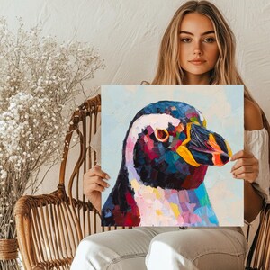 May include: Square canvas art featuring a colorful, impressionistic painting of a penguin's head. The artwork uses a palette of blues, blacks, reds, yellows, and pinks. The penguin's eye is a focal point, with a bright orange iris.