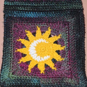 Könnte beinhalten: Handgefertigtes gehäkeltes Quadrat mit einer gelben Sonne und einem weißen Halbmond. Der Hintergrund hat einen Farbverlauf aus Lila, Türkis und Schwarz. Die strukturierte Häkelarbeit zeigt ein himmlisches Thema.