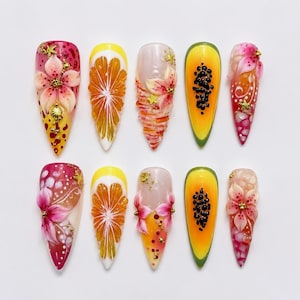 May include: A set of ten stiletto-shaped press-on nails featuring intricate 3D designs. The collection includes hand-painted floral patterns, citrus fruit slices, and papaya motifs in vibrant shades of pink, yellow, orange, and green with gold accents.