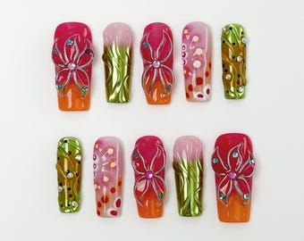 May include: A set of ten artificial nails with a variety of designs. The nails feature a gradient of orange to pink, with floral and abstract patterns. Some nails have silver accents and rhinestones.