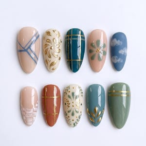 May include: A collection of ten almond-shaped artificial nails, each with a unique design. The designs include geometric patterns, floral motifs, and cloud patterns, in colors like blue, gold, and various shades of pink and green.